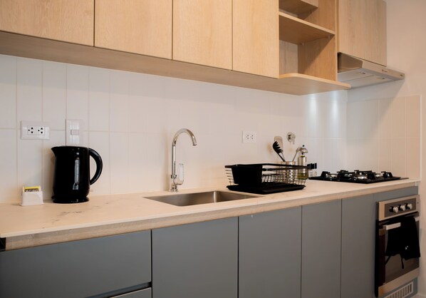 Une cuisine moderne avec des meubles gris, un évier en acier inoxydable, une machine à café noire et une cuisinière à gaz.