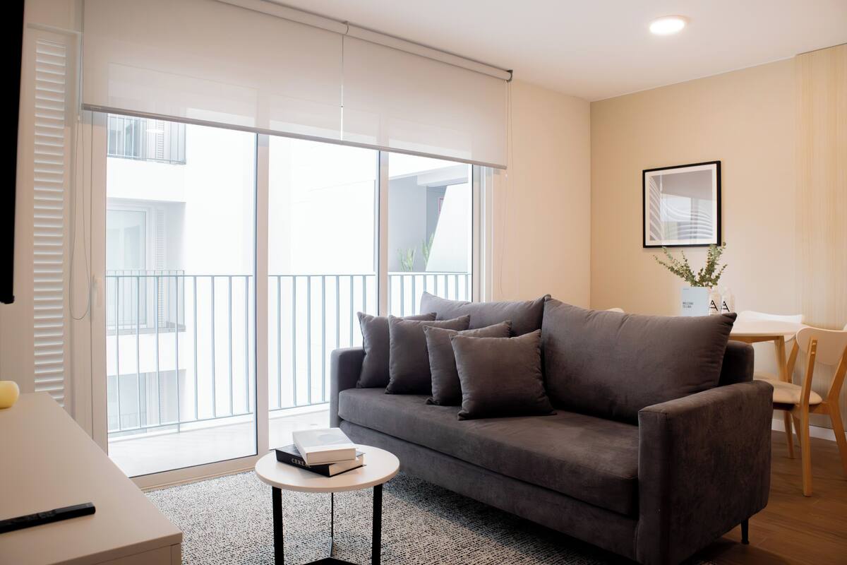 A modern living room with a grey sofa, a small round table, and a white wall with a framed picture.