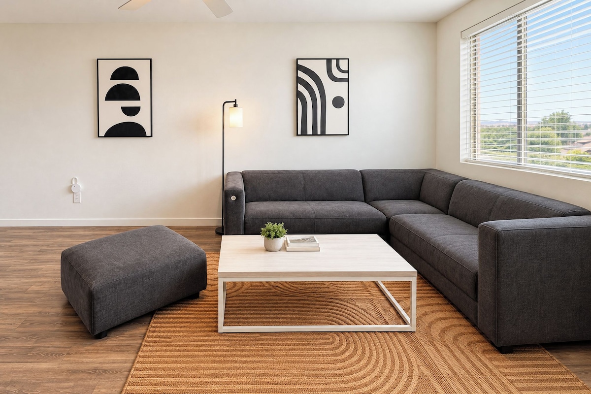A modern living room with a sectional sofa, a small ottoman, a coffee table, and two abstract wall art pieces.