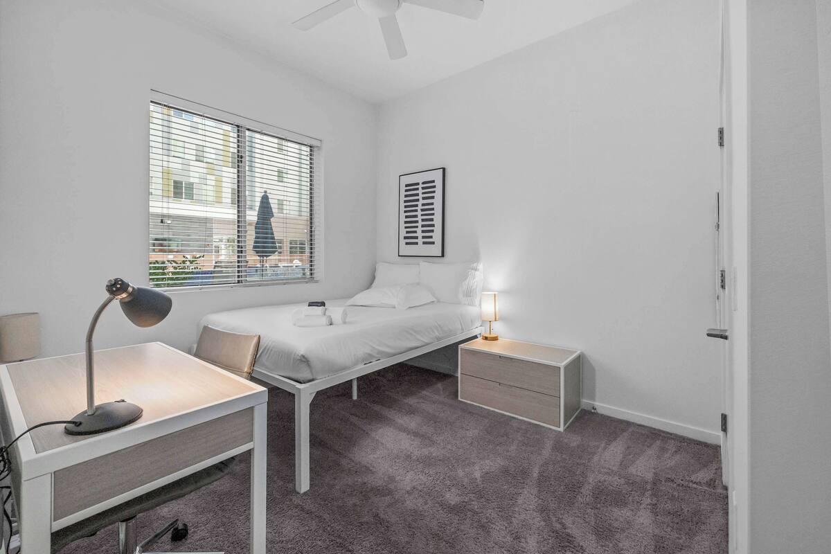 A bedroom with a bed, bedside tables, a desk, and a window with blinds.