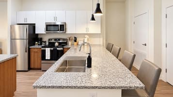 Una cocina moderna con electrodomésticos de acero inoxidable, encimera de granito y comedor con sillas.