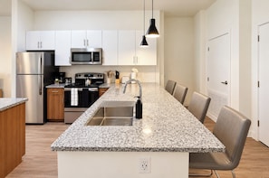 A modern kitchen with stainless steel appliances, a granite countertop, and a dining area with chairs. - Boulevard Stays - Tempe ASU (Tempe)