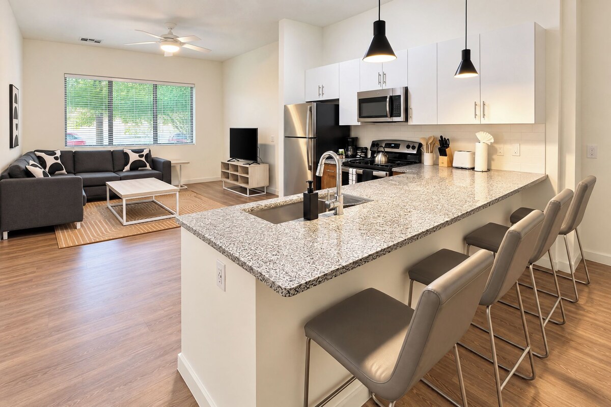 A modern kitchen with a central island, bar stools, and a dining area with a sofa and coffee table.