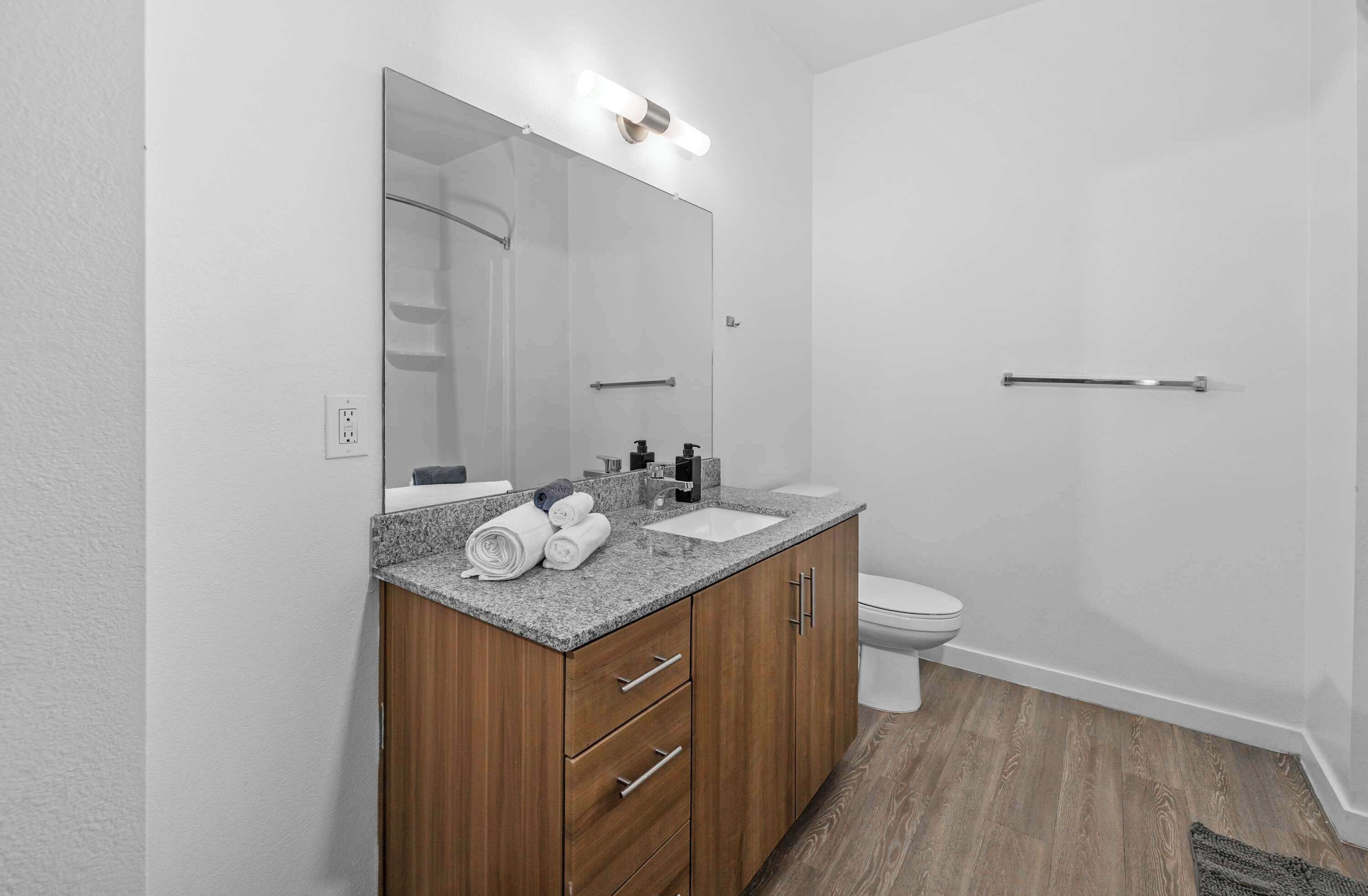 A modern bathroom with a granite countertop, wooden vanity, a large mirror, and a toilet.