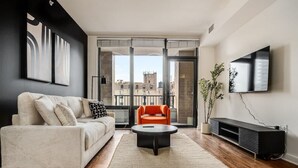 A modern living room with a sofa, a round coffee table, a TV, and a balcony with a view of buildings. - Boulevard Stays - River North (Chicago)