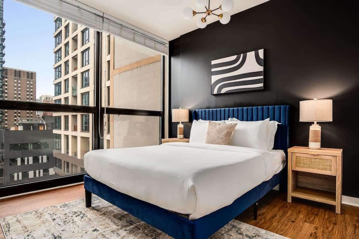 A modern bedroom with a large bed, two bedside tables, and a city view.