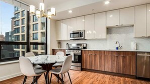 A modern kitchen with white cabinets, a marble countertop, and a dining area with a table and chairs. - Boulevard Stays - River North (Chicago)