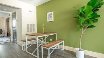 A dining area with a wooden table and benches, a potted plant, and a green wall with a framed picture.