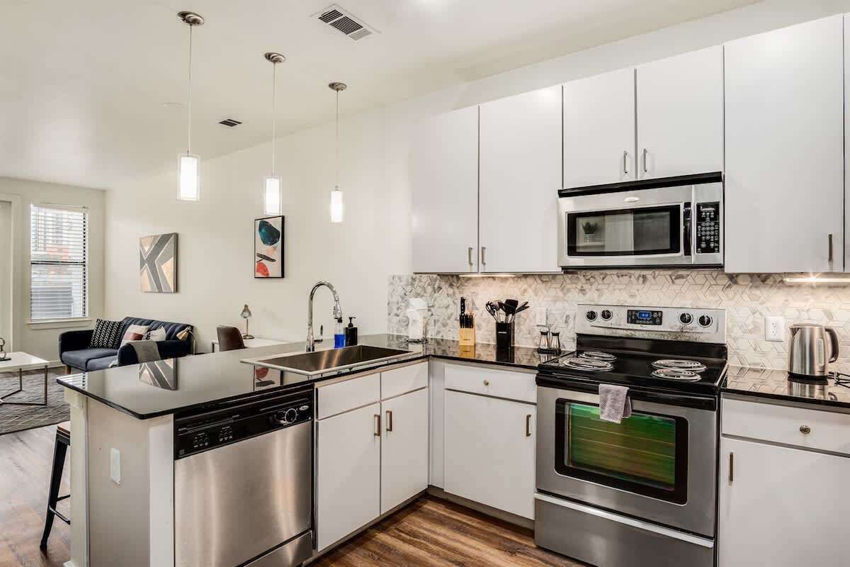 A modern kitchen with stainless steel appliances, white cabinetry, and pendant lighting.