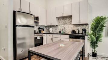 A modern kitchen with white cabinets, a stainless steel refrigerator, a built-in oven, and a coffee maker.