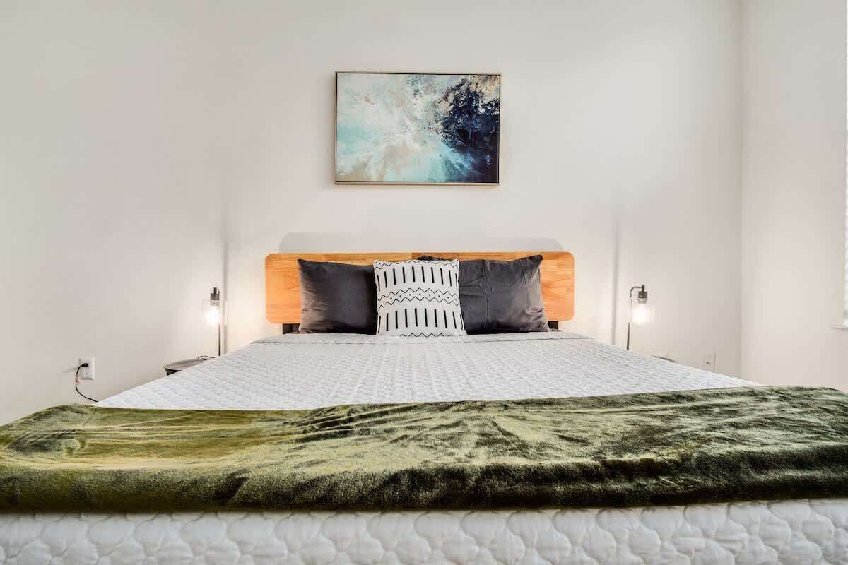 A bed with a white quilt, a green blanket, and two pillows with a geometric pattern.