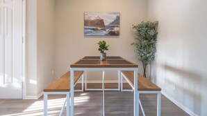 A room with a wooden table and benches, a painting of a coastal landscape, and a potted plant. - Irving Apartments (Irving)