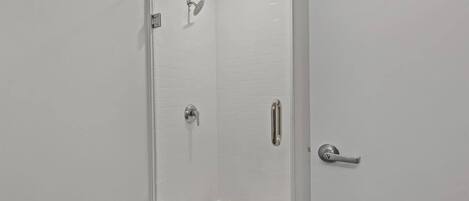 A modern shower area with a glass door, a handheld showerhead, a wall-mounted faucet, and a handheld showerhead.