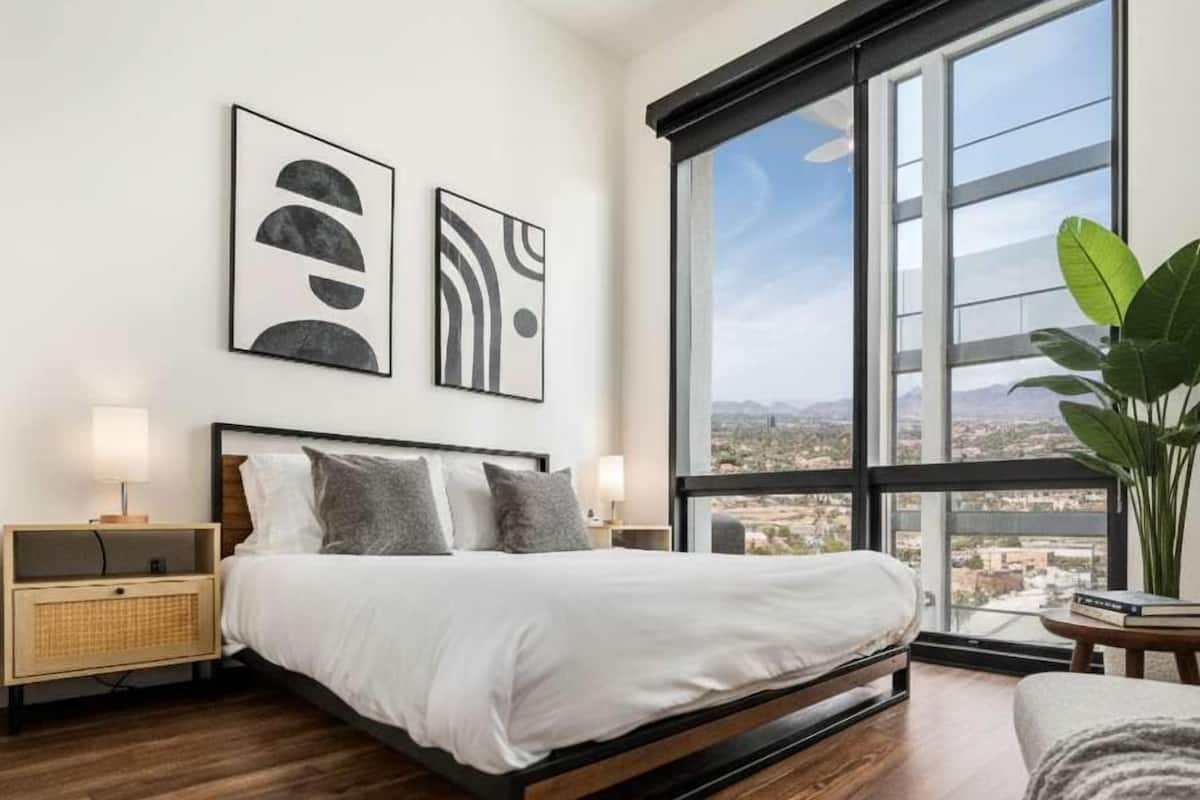 A modern bedroom with a large bed, two bedside tables, and a view of a cityscape through a large window.