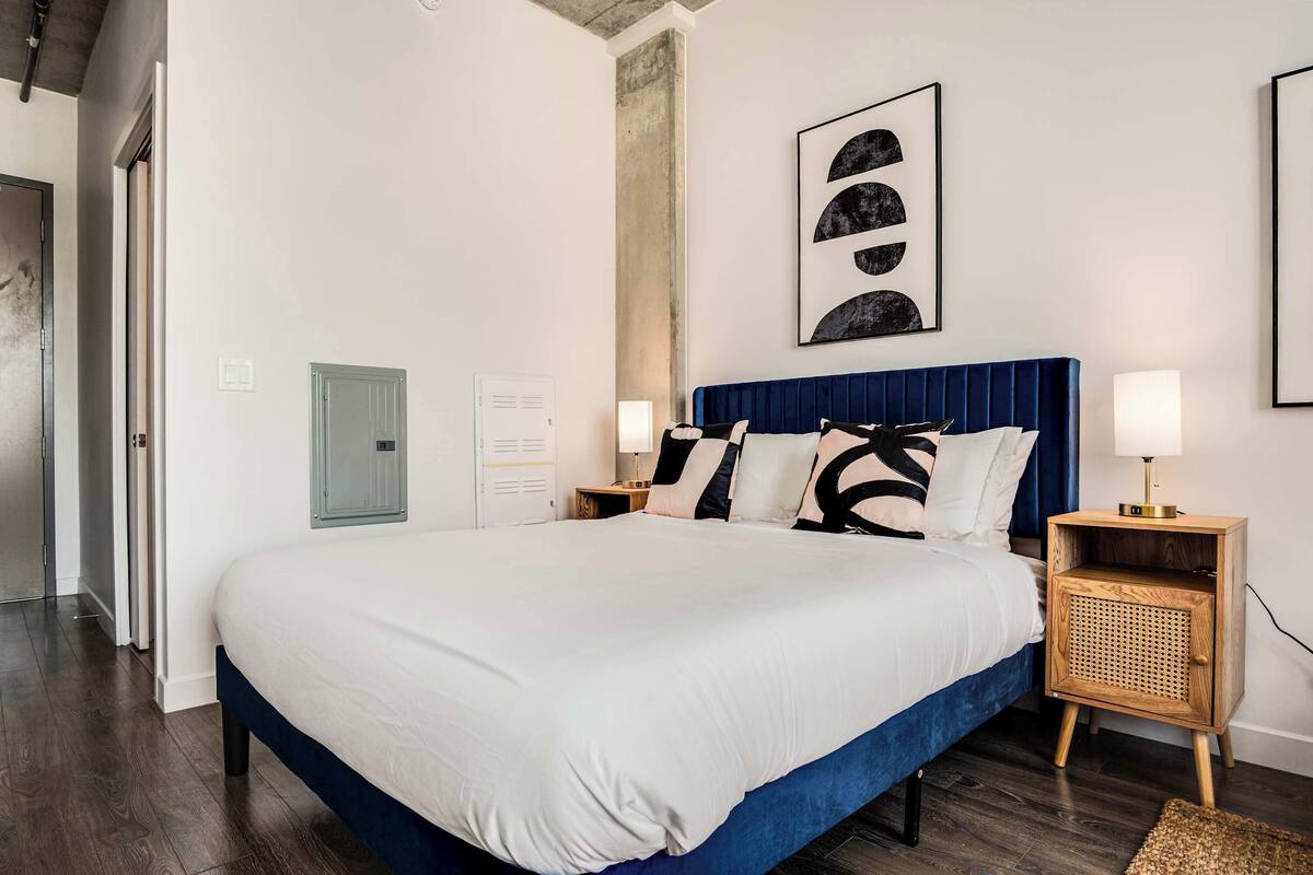 A bedroom with a large bed, a headboard, bedside tables, a lamp, and a wall-mounted artwork.