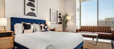 Habitación de hotel moderna con una cama grande, un sofá, un escritorio y un amplio ventanal con vistas a la ciudad.