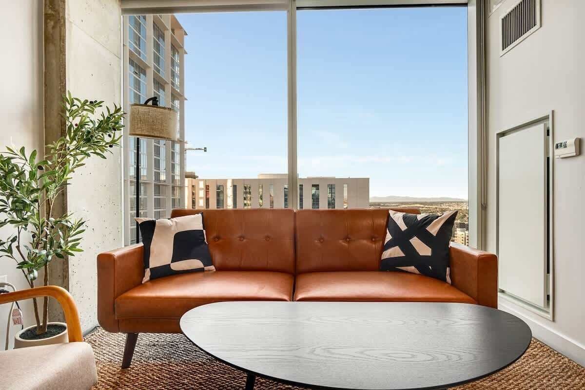 A modern living room with a leather sofa, a round coffee table, and a large window offering a city view.