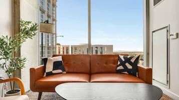 A modern living room with a leather sofa, a round coffee table, and a large window offering a city view.