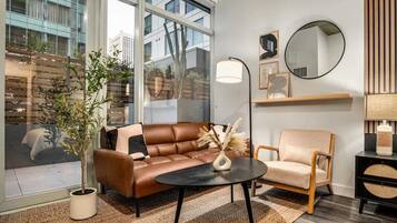 A modern living room with a leather sofa, a round coffee table, a side chair, a large window, and a mirror on the wall.