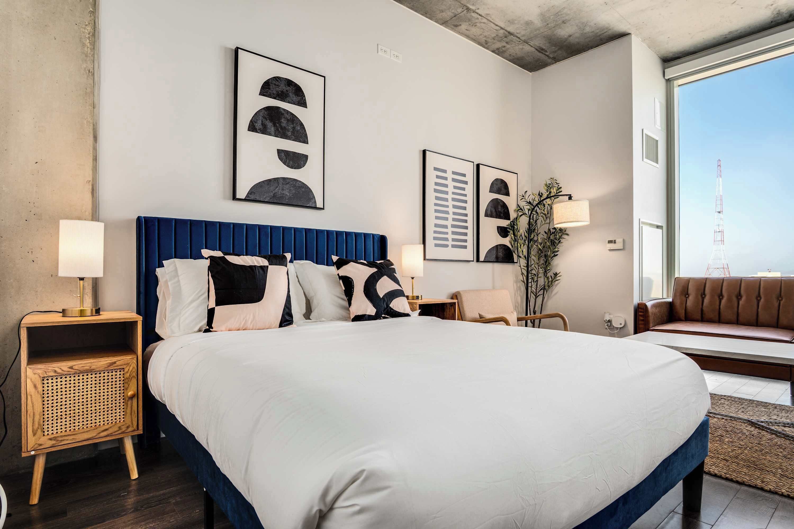 Quarto de hotel moderno com uma cama grande, duas mesas de cabeceira, um sofá e obras de arte nas paredes.