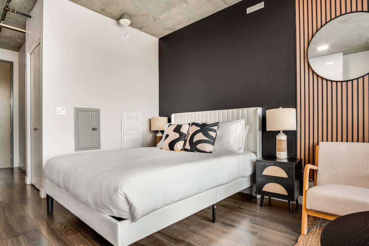 A modern bedroom with a large bed, bedside tables, a chair, and a mirror.