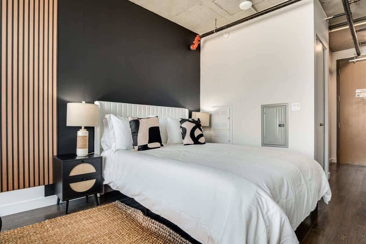 A modern bedroom with a large bed, a nightstand, a lamp, and a door.