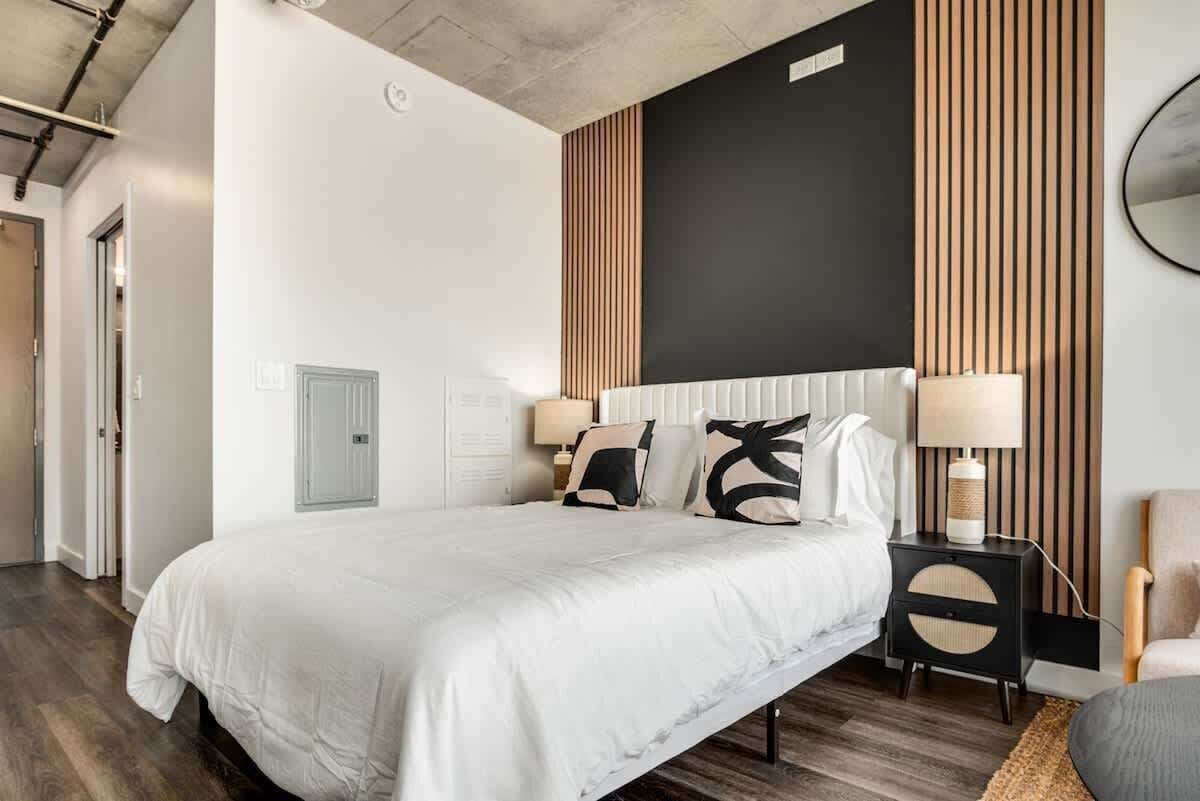A modern bedroom with a large bed, a wooden accent wall, and a black headboard.