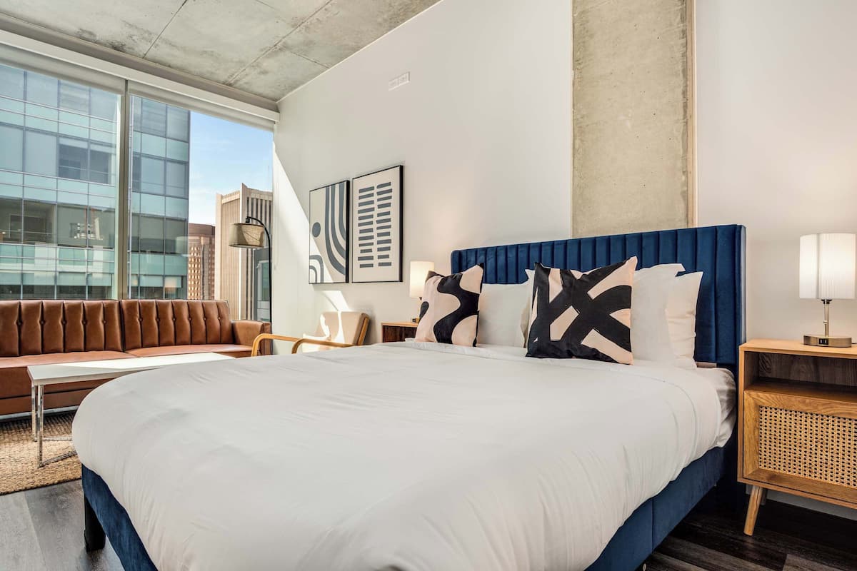 A modern hotel room with a large bed, a sofa, and a view of the city.