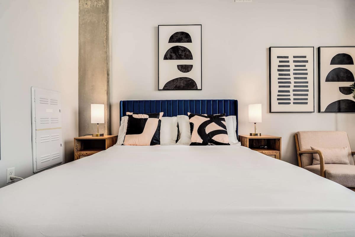 A hotel room with a large bed, two bedside tables with lamps, a chair, and artwork on the walls.
