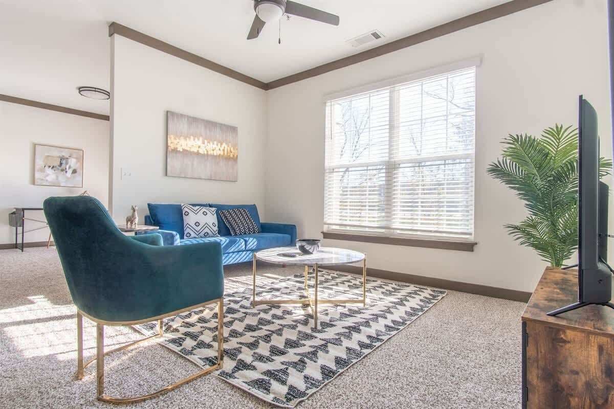 A living room with a blue sofa, a teal armchair, a coffee table, and a television on a wooden stand.
