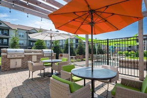Un patio al aire libre con una parrilla, muebles de mimbre y sombrillas.