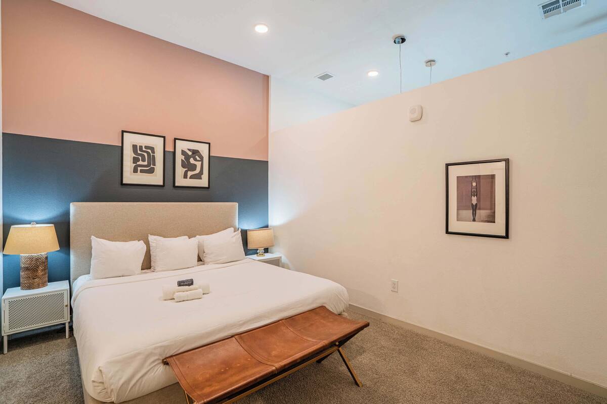 A hotel room with a bed, bedside tables, a bench, and wall art.