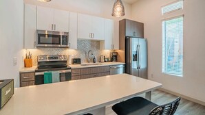 A modern kitchen with stainless steel appliances, a large island, and pendant lighting. - Boulevard Stays - Roosevelt Row (Phoenix)