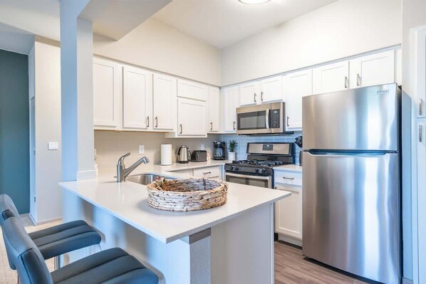 A modern kitchen with white cabinets, stainless steel appliances, and a central island with seating. - Boulevard Stays - Pflugerville (Austin)