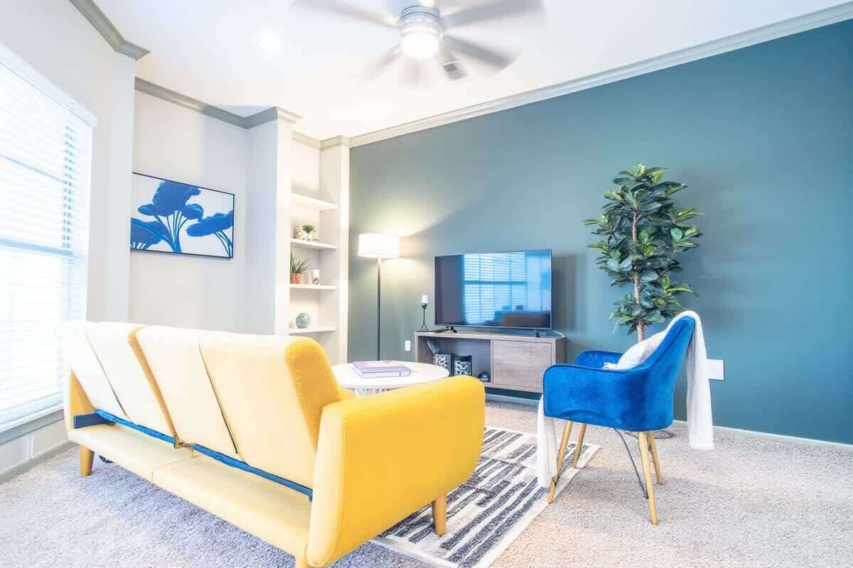Una sala de estar con un sofá amarillo, un sillón azul, un televisor y una planta.