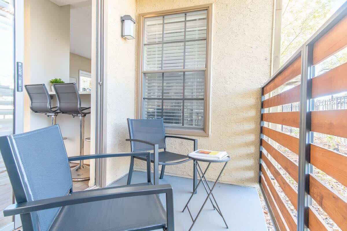 Ein kleiner Außenbereich mit zwei Stühlen und einem Tisch, ein Fenster mit Jalousien und ein Holzzaun.