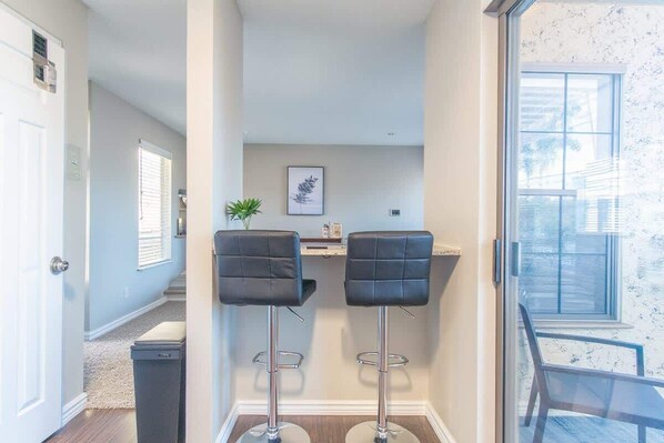 A modern kitchen with two bar stools, a window, and a plant. - Boulevard Stays - North Dallas (Dallas)
