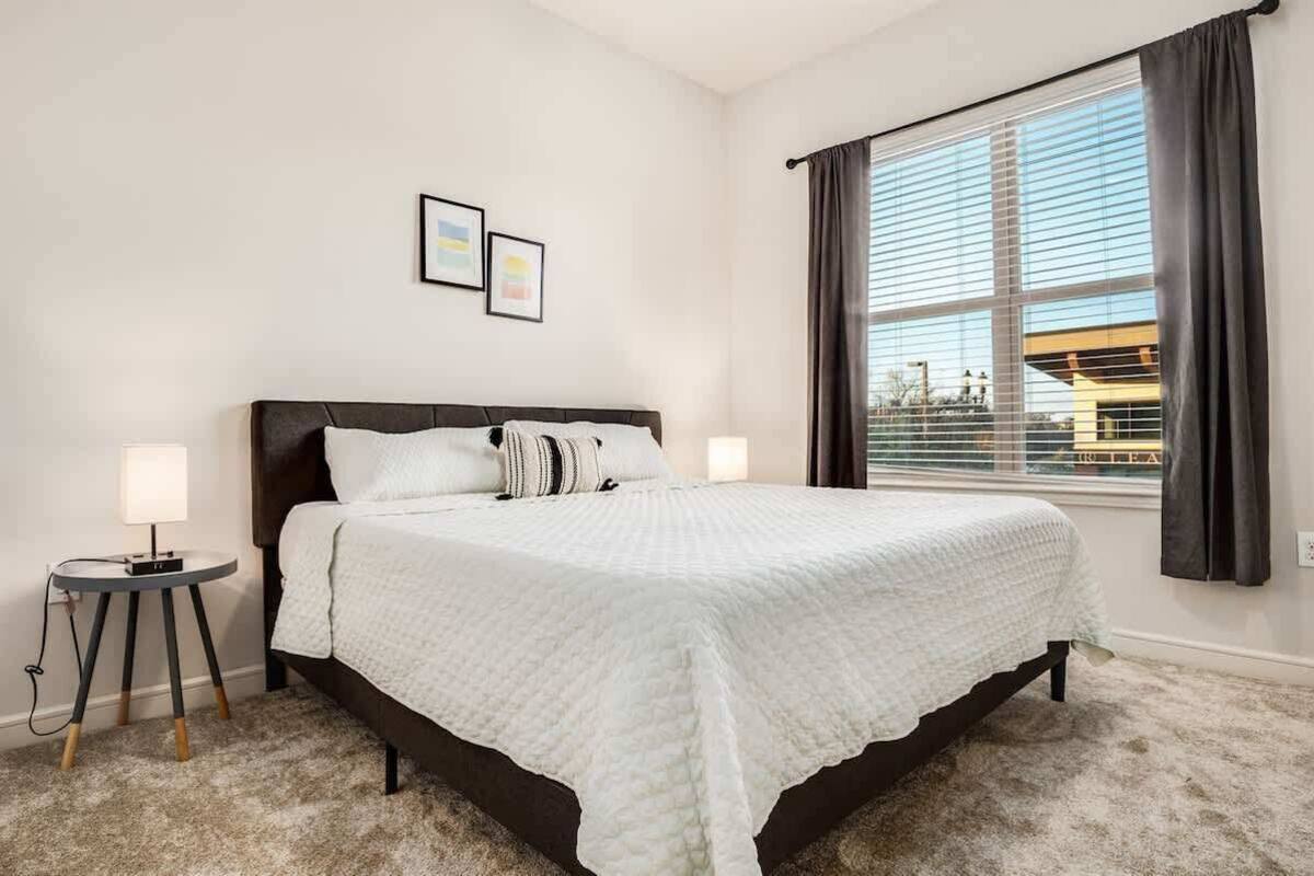 Un dormitorio con una cama grande, dos lámparas de noche, una mesita y una ventana con cortinas.