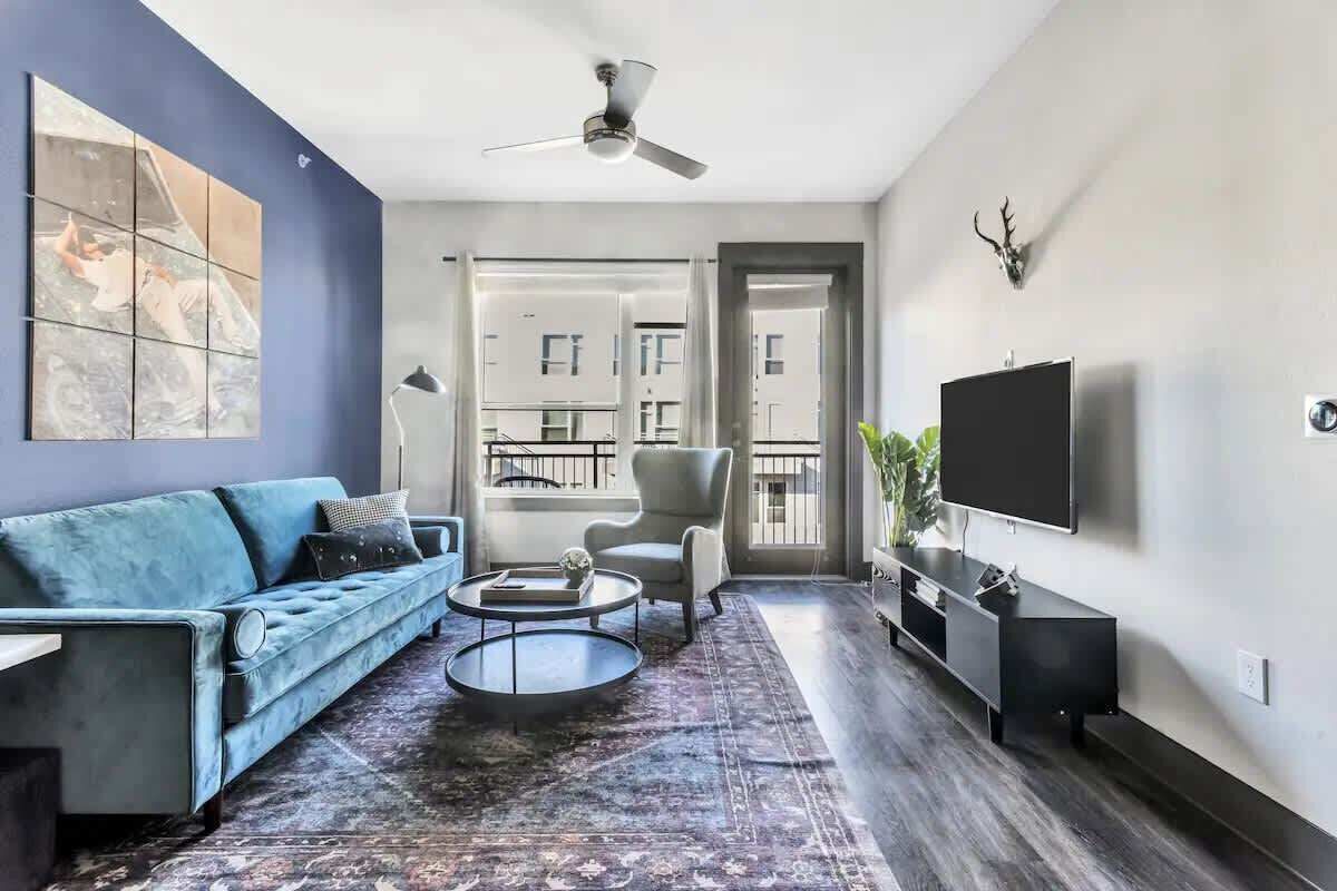 A modern living room with a blue sofa, a coffee table, a TV, and a ceiling fan.