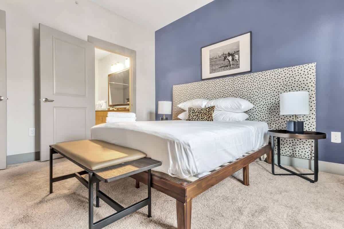 Une chambre à coucher avec un lit, des tables de chevet, un banc, un miroir et un tableau encadré accroché au mur.