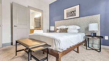 Une chambre à coucher avec un lit, des tables de chevet, un banc, un miroir et un tableau encadré accroché au mur.