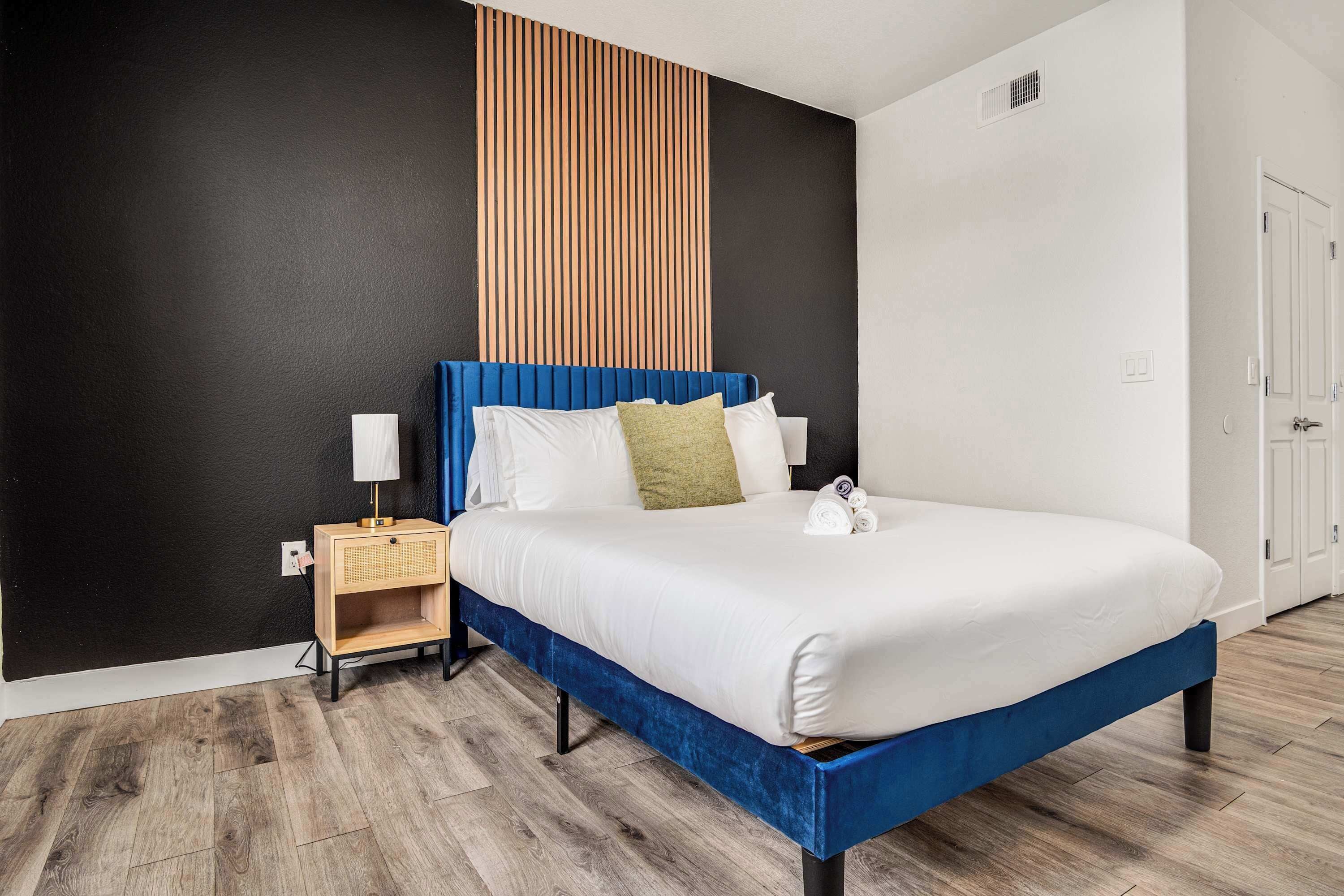 A modern hotel room with a large bed, a nightstand, a lamp, and a wooden panel wall.