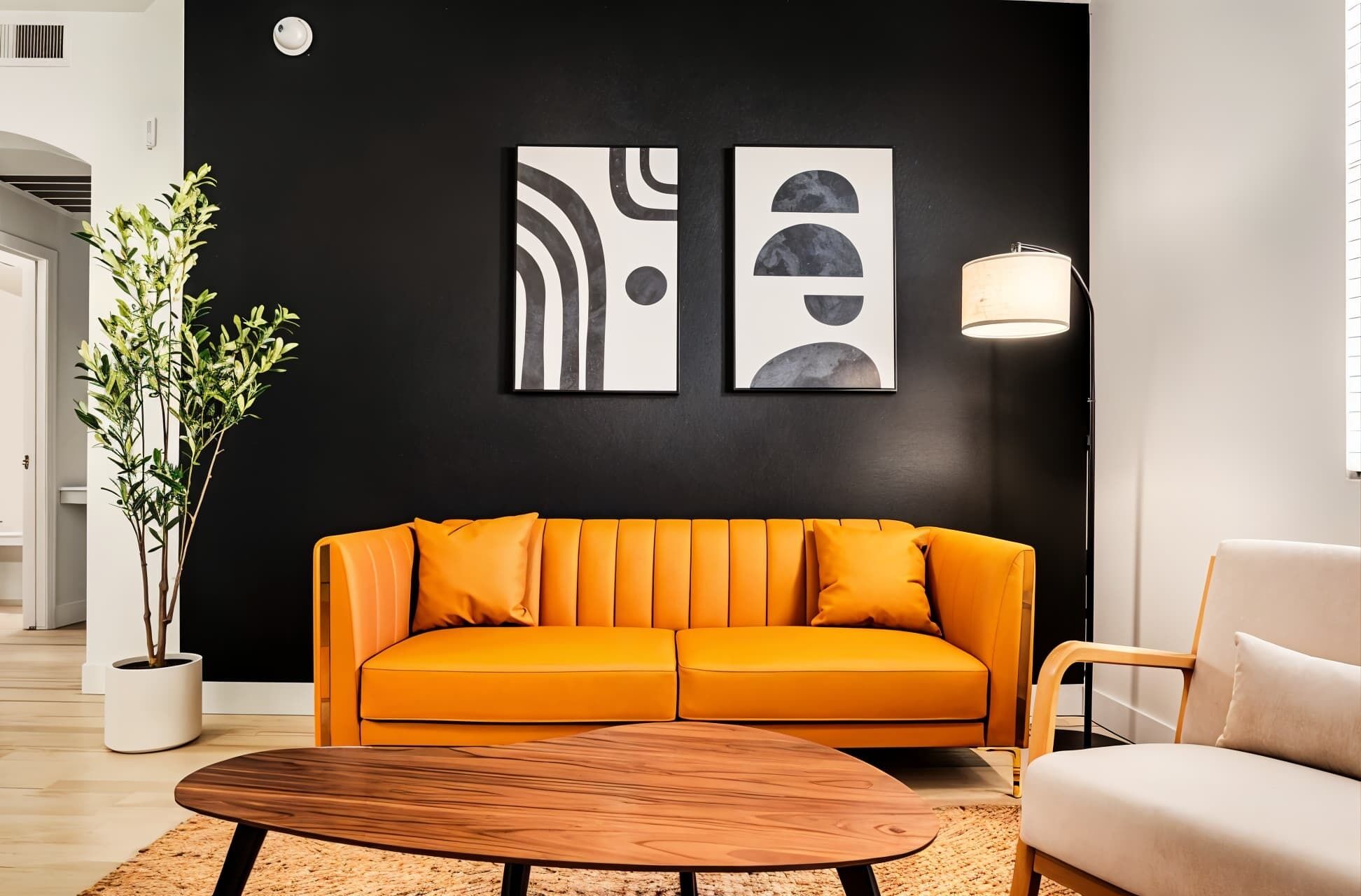 Ett modernt vardagsrum med en svart vägg, två abstrakta målningar, en orange soffa, ett soffbord i trä, en golvlampa och en krukväxt.