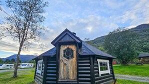 A log cabin with a hexagonal window, surrounded by a grassy area and mountains in the background. - Awesome home in Røldal with WiFi (Røldal)