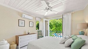 A bedroom with a bed, a ceiling fan, a dresser, a chair, and a view of greenery outside.