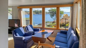 A room with a large window overlooking a lake, two blue sofas, a wooden table, and a television. - Awesome home in Kolbjørnsvik with house sea view (Kolbjørnsvik)