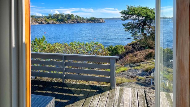 A wooden deck with a bench overlooking a calm body of water, surrounded by greenery and rocky terrain. - Awesome home in Kolbjørnsvik with house sea view (Kolbjørnsvik)