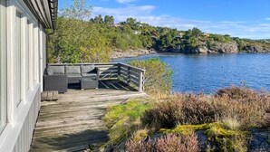 A wooden deck with outdoor furniture overlooking a lake, surrounded by greenery and houses in the background. - Awesome home in Kolbjørnsvik with house sea view (Kolbjørnsvik)