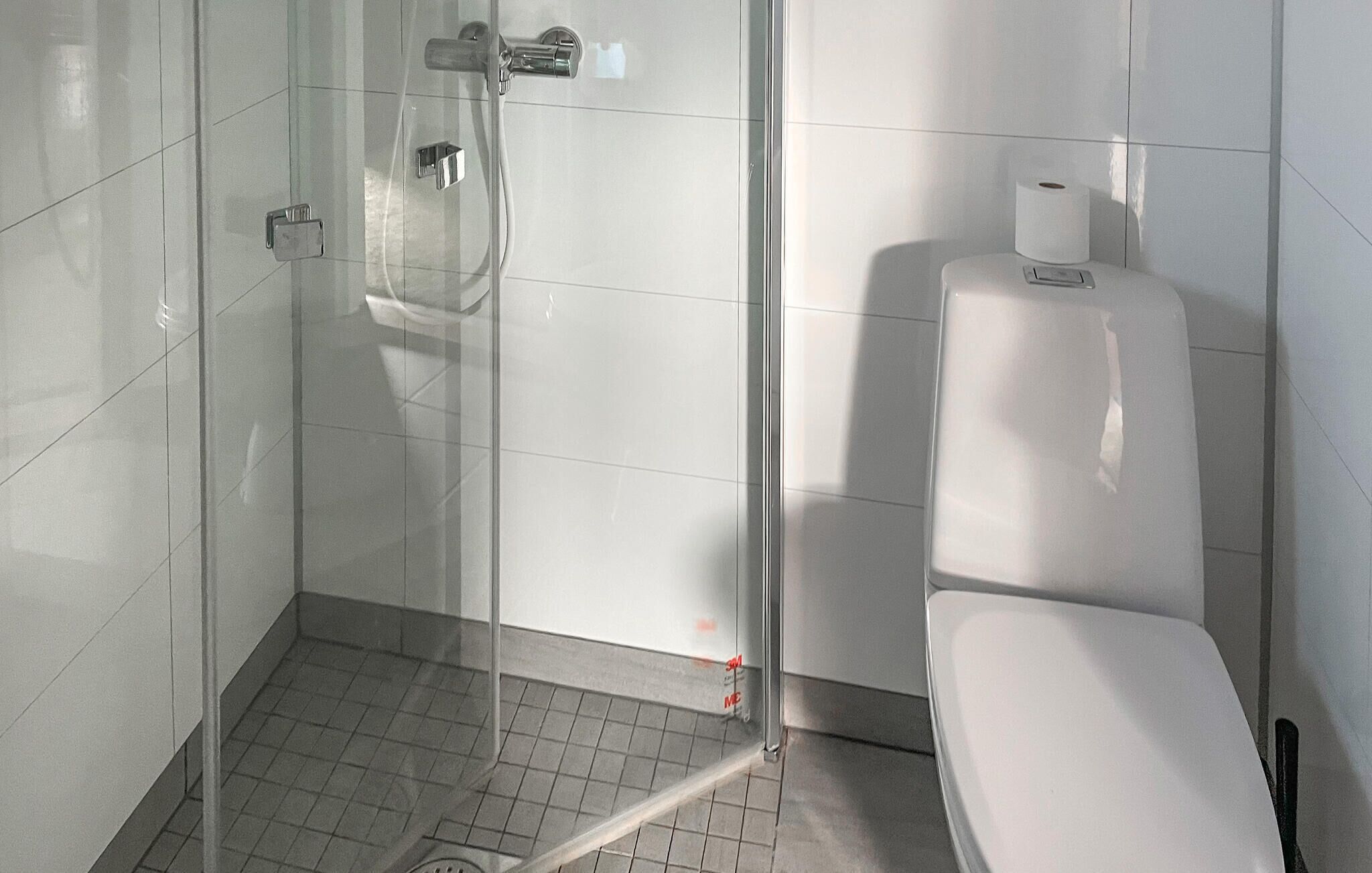 A modern bathroom with a glass shower enclosure, a toilet, and a paper towel dispenser.