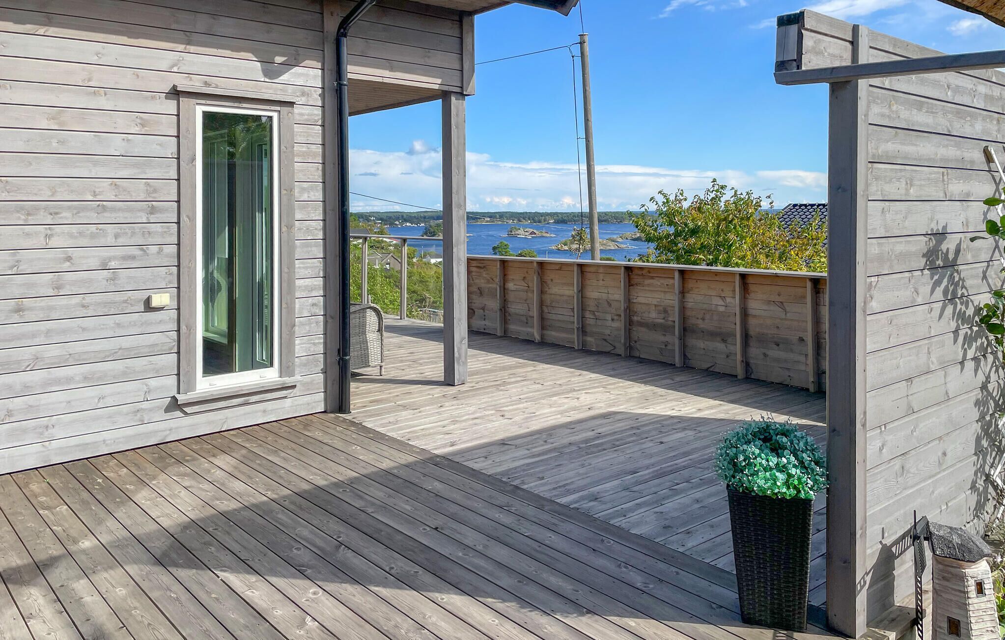 A wooden deck with a view of the water, a small garden, and a wooden structure.